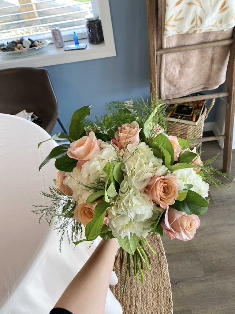 Bridal bouquet of blush roses, white hydrangea and greenery held indoors