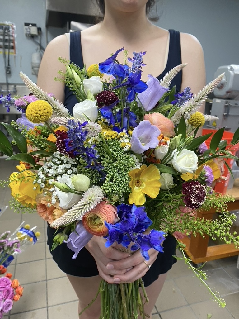 Large mixed bouquet of blue delphinium, yellow billy buttons and white blooms held in workroom