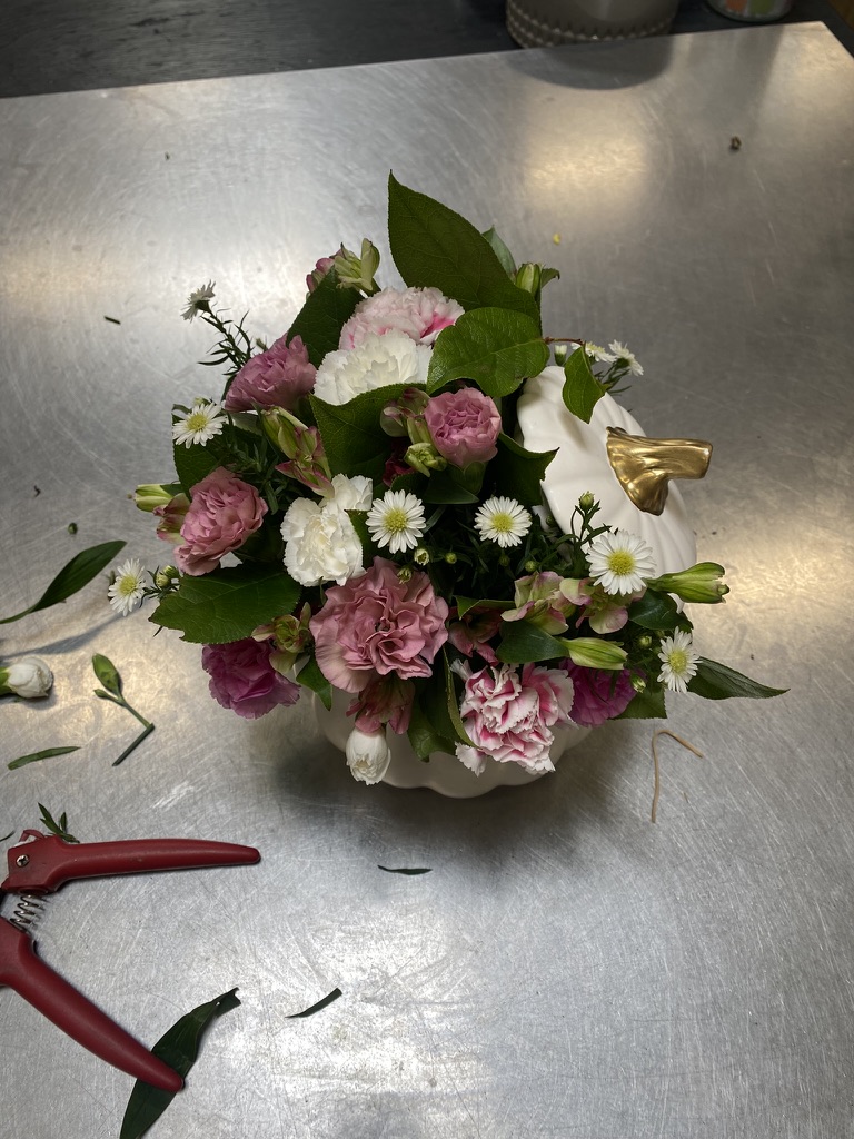 Pink carnations and white daisies in small white pumpkin vase on steel worktable