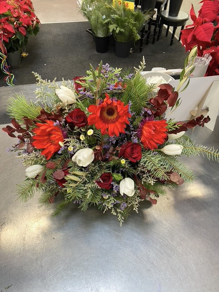 Low centerpiece with red gerbera daisies, roses, white tulips, and evergreen greenery
