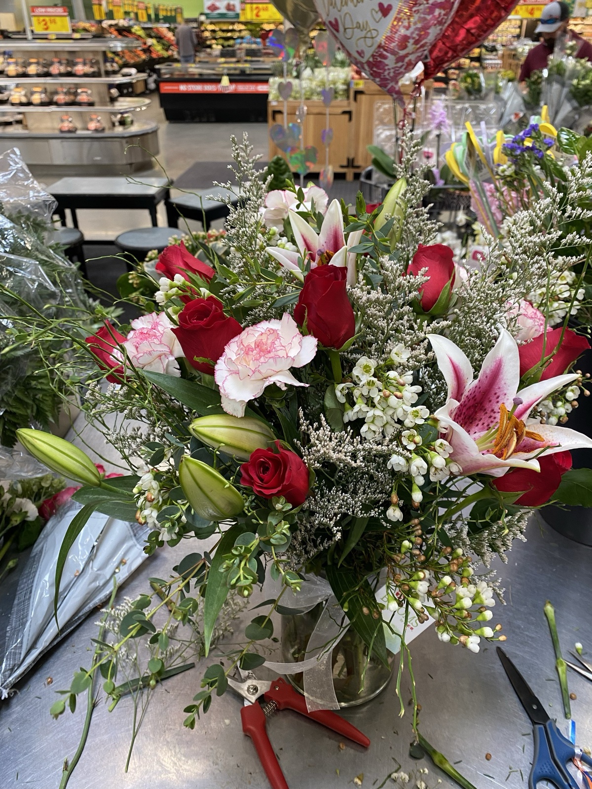 Vase arrangement of red roses, pink carnations, and stargazer lilies on florist worktable