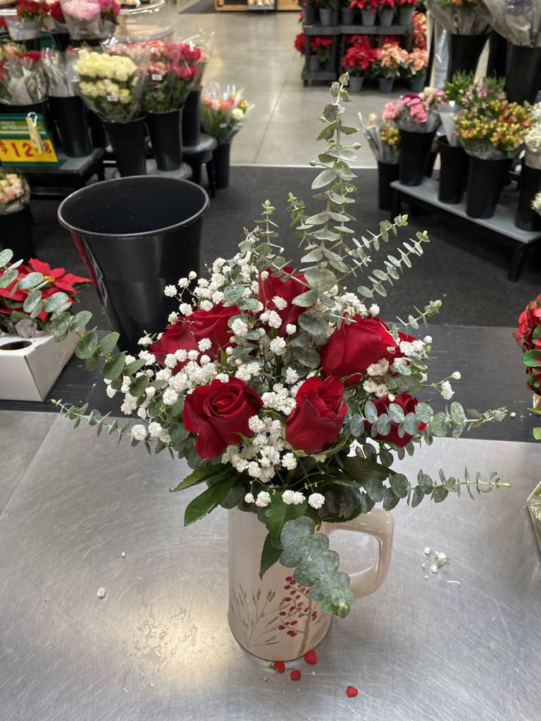 Red roses with baby's breath and eucalyptus in cream ceramic pitcher on shop counter