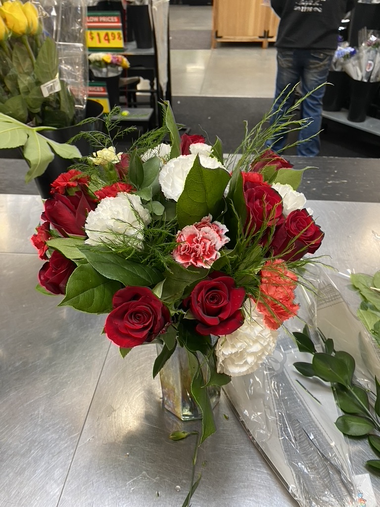 Red roses and white carnations with greenery in glass vase on metal counter